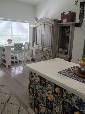 Un coin repas avec une table et des chaises blanches, un meuble contenant des objets décoratifs et un mur de crédence orné de motifs.