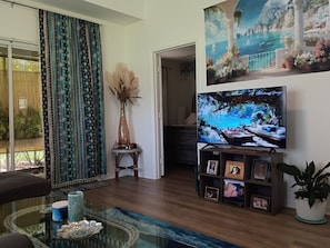 A living room with a television, a sofa, a coffee table, and a bookshelf with framed photos. - Peaceful one bedroom Villa with Mediterranean decor (Palm Harbor)