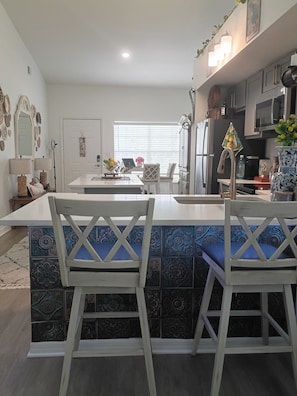 A modern kitchen with a central island, white cabinetry, and a dining area with patterned tiles and white chairs. - Peaceful one bedroom Villa with Mediterranean decor (Palm Harbor)