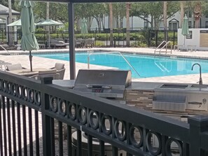 A poolside area with a grill, lounge chairs, and umbrellas. - Peaceful one bedroom Villa with Mediterranean decor (Palm Harbor)