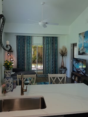 A modern kitchen with a white countertop, a stainless steel sink, a ceiling fan, and a dining area with a table and chairs. - Peaceful one bedroom Villa with Mediterranean decor (Palm Harbor)