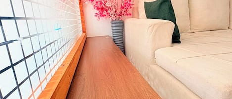 Une pièce avec un banc en bois, un canapé beige, un vase avec une fleur rose et une citation encadrée accrochée au mur.