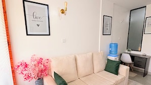 A living room with a beige sectional sofa, a small side table, a potted plant, and a water dispenser. - Cozy one bedroom apartment (Ongata Rongai)