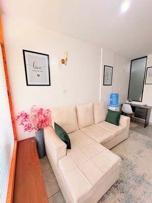 A living room with a beige sectional sofa, a small side table, a potted plant, and a water dispenser. - Cozy one bedroom apartment (Ongata Rongai)