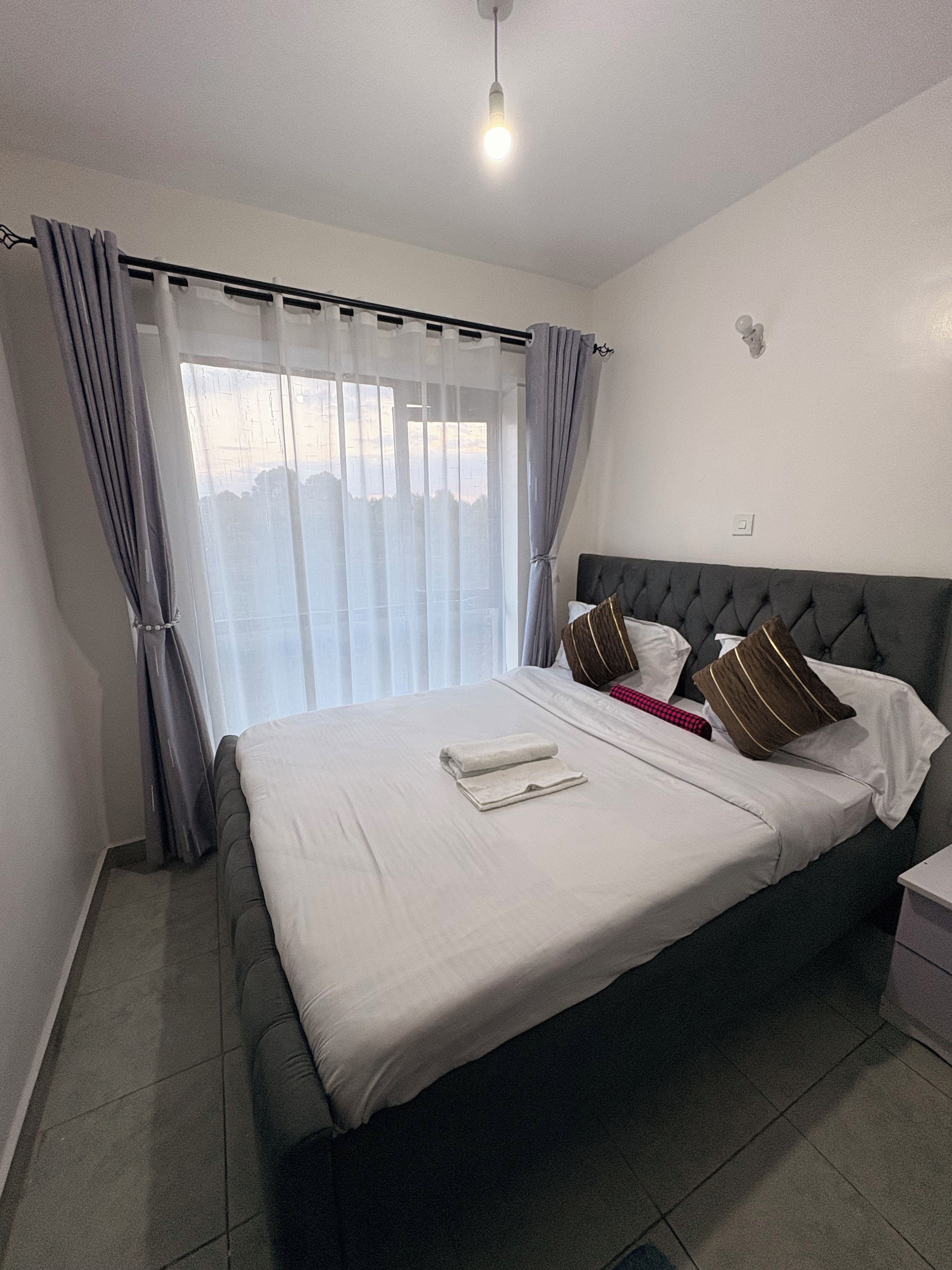 A hotel room with a large bed, curtains, a bedside table, and a nightstand.