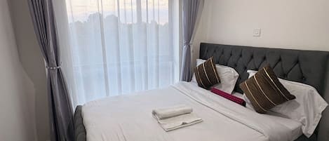 A hotel room with a large bed, curtains, a bedside table, and a nightstand.