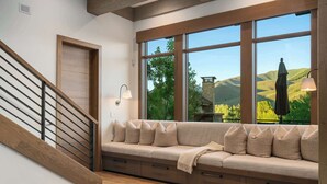 A modern interior with a wooden staircase, a built-in bench with cushions, and a large window offering a view of hills. - Abode at White Clouds, hot tub, Sun Valley (Sun Valley)