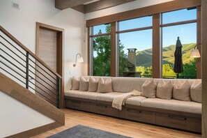 A modern interior with a wooden staircase, a built-in bench with cushions, and a large window offering a view of hills. - Abode at White Clouds, hot tub, Sun Valley (Sun Valley)