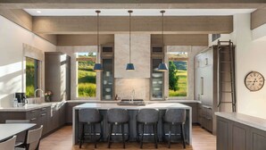A modern kitchen with a central island, bar stools, a built-in oven, and a view of a green landscape through large windows. - Abode at White Clouds, hot tub, Sun Valley (Sun Valley)