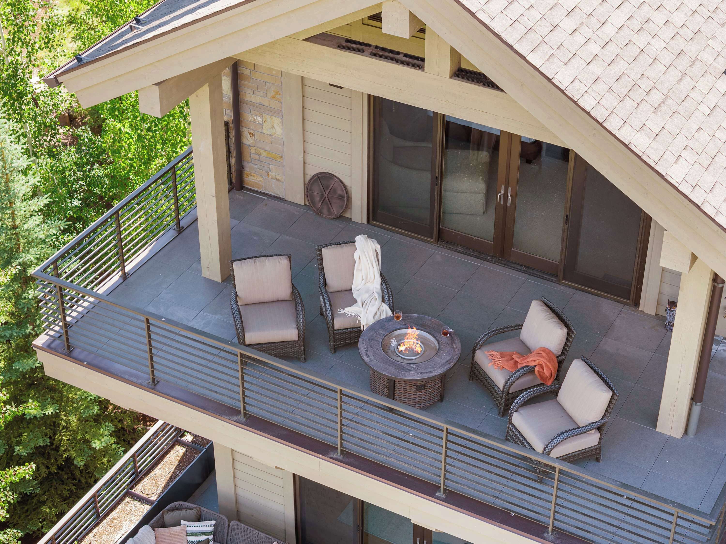 A covered outdoor seating area with wicker furniture, a fire pit, and a view of a house with a tiled roof.