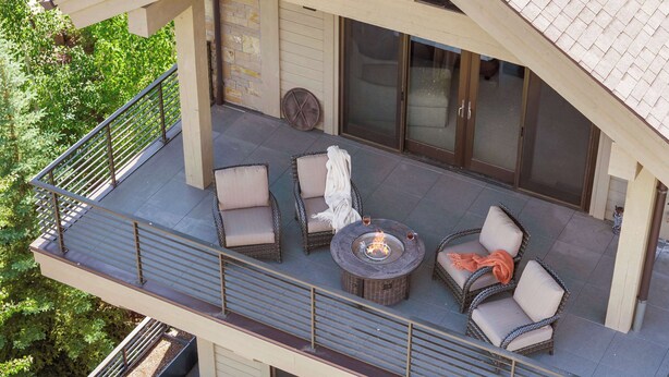 A covered outdoor seating area with wicker furniture, a fire pit, and a view of a house with a tiled roof. - Abode at White Clouds, hot tub, Sun Valley (Sun Valley)