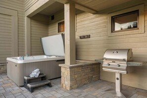Eine Außenpatio mit Whirlpool, Grill und Kamin aus Stein.