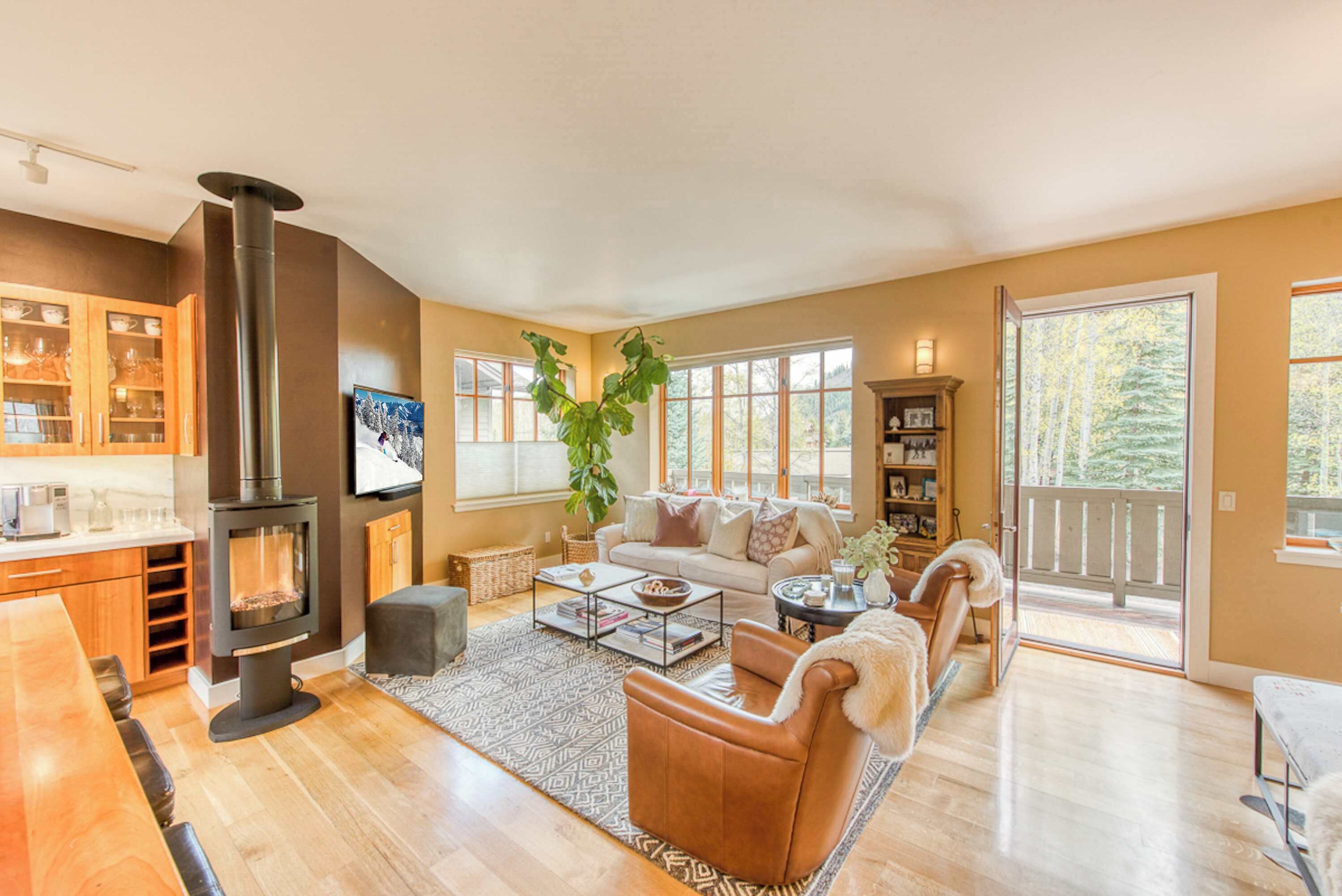 A cozy living room with a fireplace, a sofa, a coffee table, and a large window offering a view of the outdoors.