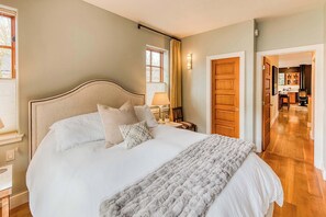 Quarto com cama grande, mesa de cabeceira, abajur e vista para o corredor.
