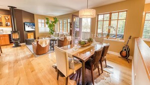 A spacious living area with a wooden dining table, chairs, a fireplace, and large windows offering views of the outdoors. - Abode at Ketchum Escape, walk to Main St, ensuites (Ketchum)