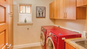 A laundry room with a red washing machine, wooden cabinets, a window with blinds, and a framed picture on the wall. - Abode at Ketchum Escape, walk to Main St, ensuites (Ketchum)