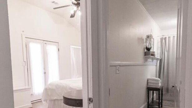 A hallway with wooden flooring, a ceiling fan, and a door leading to a room with a bed. - Schilling House (Bolivar)
