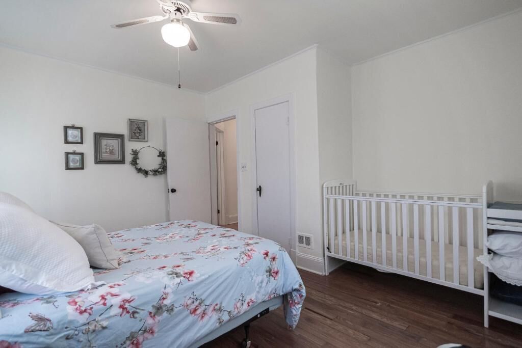 Un dormitorio con cama, cuna, ventilador de techo y una puerta.
