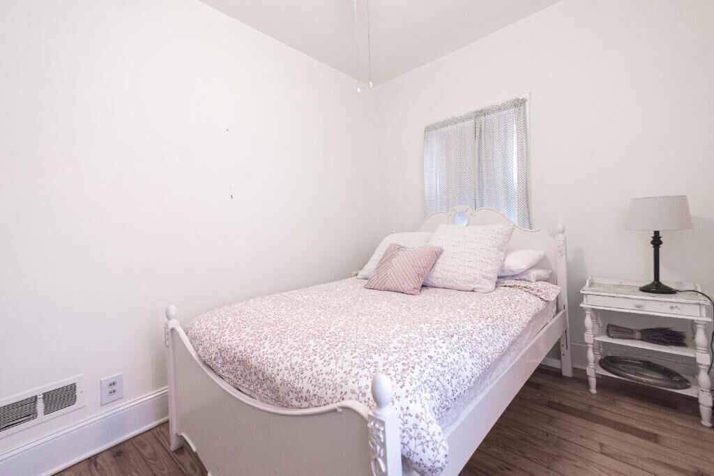 A bedroom with a single bed, a bedside table, a lamp, and a window with blinds.