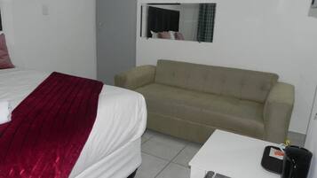 Une chambre d’hôtel avec un lit, un canapé, une petite table et un miroir au mur.