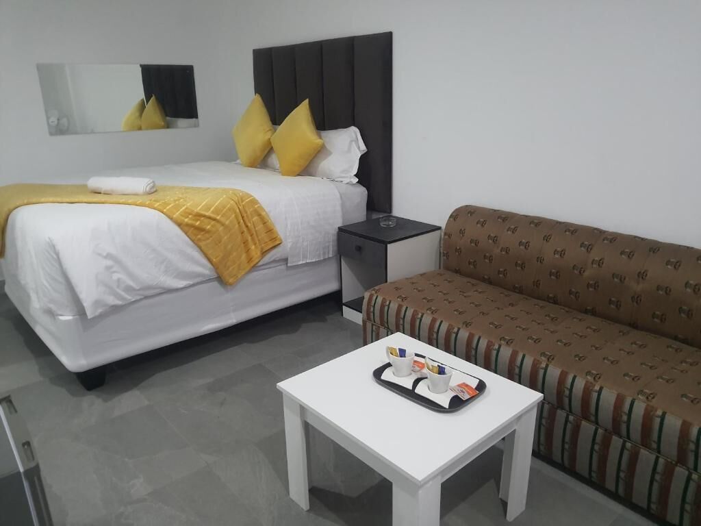 A hotel room with a bed, a nightstand, a sofa, and a small table with a tray.