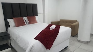 A hotel room with a large bed, a nightstand, a beige armchair, and a red throw blanket. - De Bliss Lodge (Newtown)