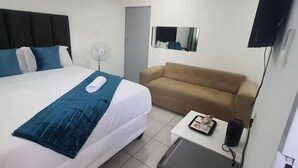 A hotel room with a bed, a sofa, a small table, a television, and a mirror. - De Bliss Lodge (Newtown)