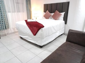 A hotel room with a bed, a nightstand, a lamp, and a window with curtains. - De Bliss Lodge (Newtown)