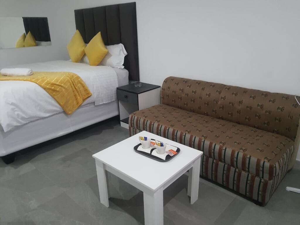 Quarto de hotel com cama, sofá, mesa de cabeceira com um serviço de objetos e um criado-mudo.