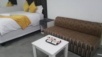 Quarto de hotel com cama, sofá, mesa de cabeceira com um serviço de objetos e um criado-mudo.
