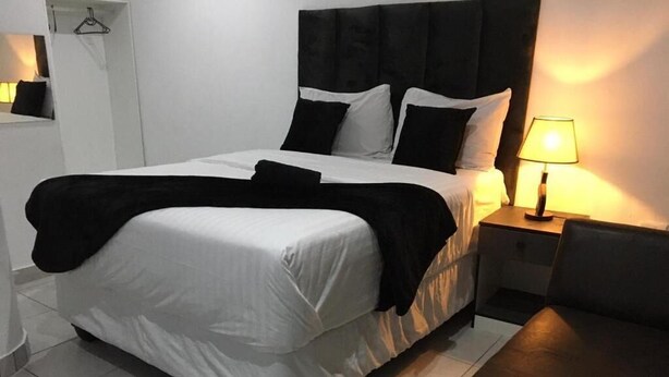 A hotel room with a bed, bedside table, lamp, and a chair. - De Bliss Lodge (Newtown)