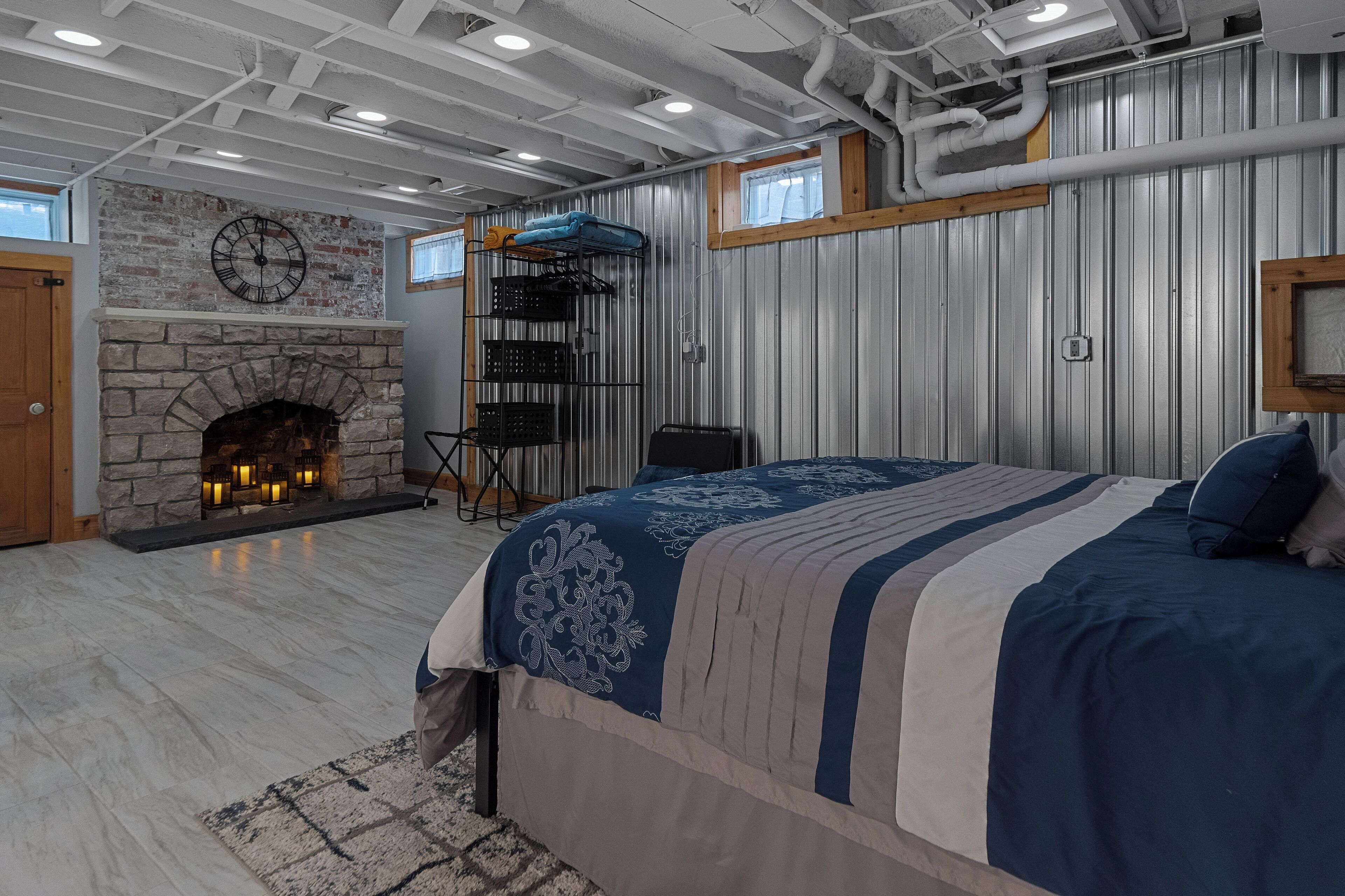 Un dormitorio con chimenea de piedra, una cama con ropa de cama estampada y una estantería de estructura metálica.