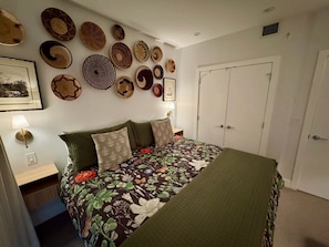 Ein Schlafzimmer mit einem blumigen Bettüberwurf, mehreren Wandkörben, einem gerahmten Bild und einer Nachttischlampe.