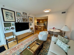 A living room with a flat-screen TV, a coffee table, a sofa, and a dining area with chairs. - Modern Luxury Kitsilano Apartment (Vancouver)