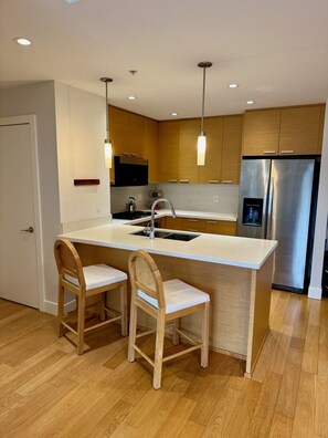 A modern kitchen with a central island, two wooden chairs, stainless steel appliances, and pendant lighting. - Modern Luxury Kitsilano Apartment (Vancouver)
