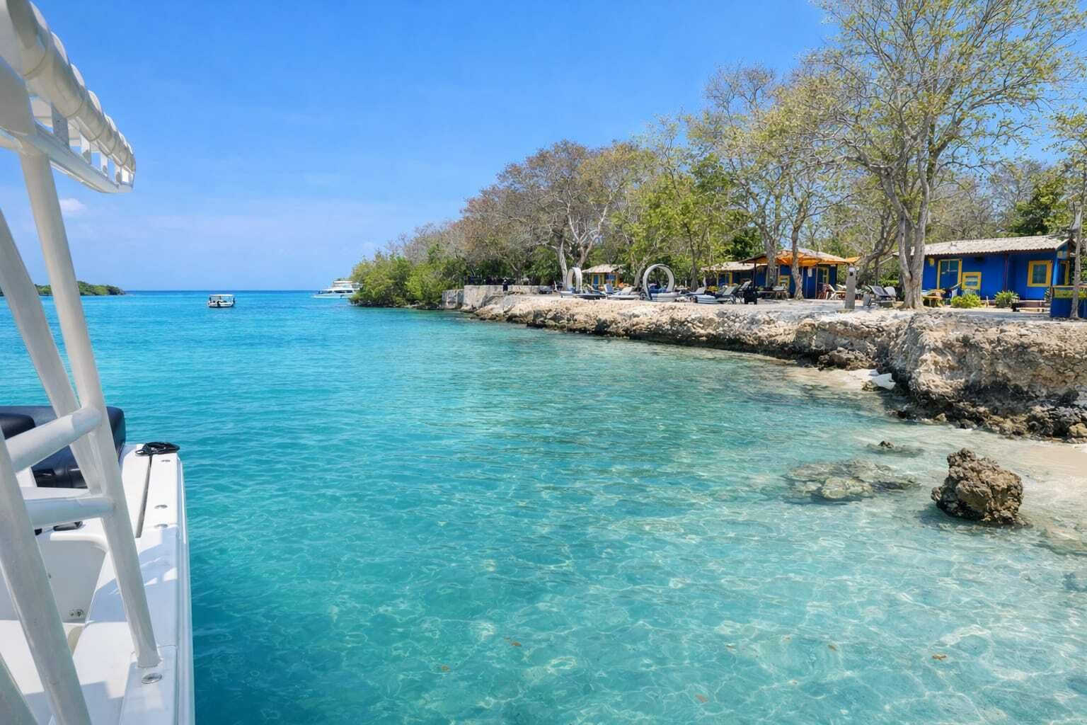 A coastal area with clear turquoise water, a rocky shoreline, and a building with blue and yellow accents.