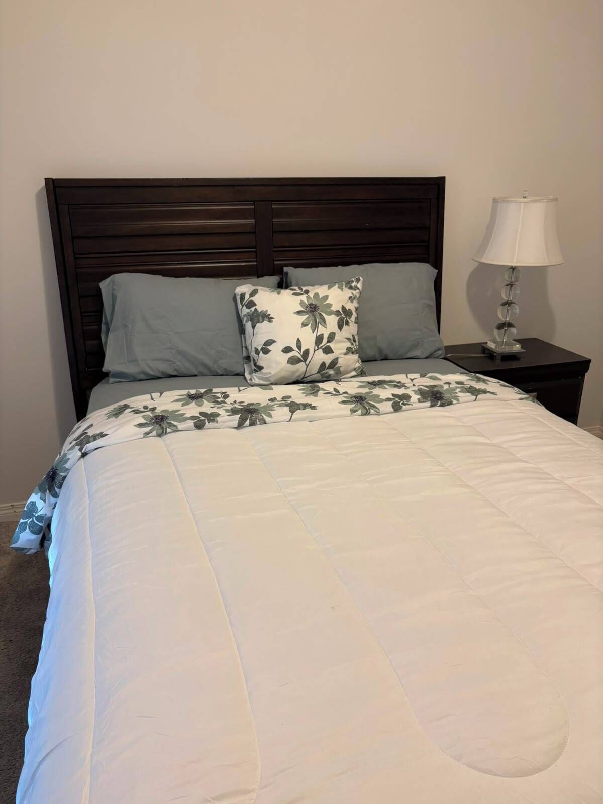 Una cama con colcha estampada, cabecera de madera oscura y una lámpara de noche sobre una mesita.