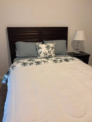 A bed with a floral bedspread, a dark wooden headboard, and a bedside lamp on a nightstand.