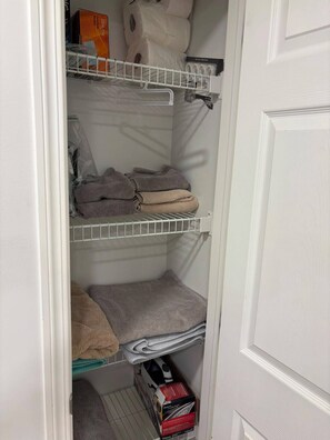A storage closet with shelves holding folded towels and a box of toiletries.