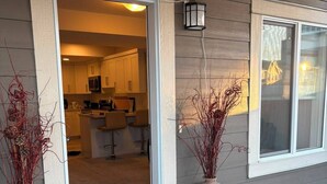 En bostadsbyggnad med en entré som består av en skjutdörr i glas, ett kök som syns inifrån och två dekorativa vaser på verandan.