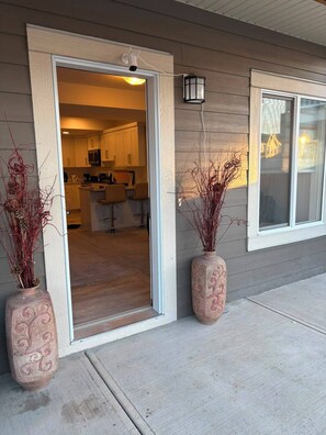 A residential building with a sliding glass door entrance, a kitchen visible inside, and two decorative vases on the porch.