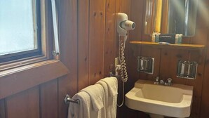 A bathroom with wooden walls, a white sink, a hairdryer, a mirror, and a window. - Cozy 1BR hotel room, Hamilton - #336 Endawonnda (Hamilton)
