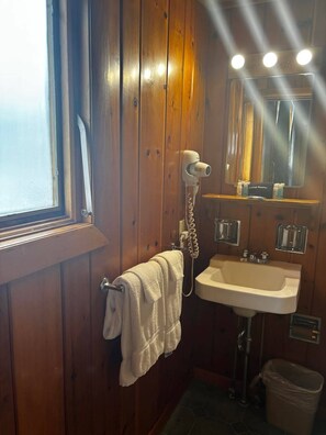 A bathroom with wooden walls, a white sink, a hairdryer, a mirror, and a window. - Cozy 1BR hotel room, Hamilton - #336 Endawonnda (Hamilton)