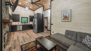 A modern kitchen with dark cabinetry, a stainless steel refrigerator, and a window with a view of greenery. - Home Sweet Smoky (Pigeon Forge)