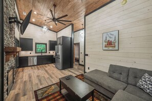 A modern kitchen with dark cabinetry, a stainless steel refrigerator, and a window with a view of greenery. - Home Sweet Smoky (Pigeon Forge)