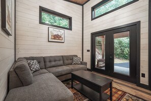 A modern interior with a sectional sofa, a small table, and a large sliding glass door leading to an outdoor area. - Home Sweet Smoky (Pigeon Forge)