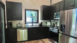 A modern kitchen with black cabinets, stainless steel appliances, a dishwasher, and a window providing natural light. - Home Sweet Smoky (Pigeon Forge)