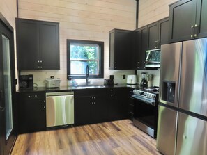 A modern kitchen with black cabinets, stainless steel appliances, a dishwasher, and a window providing natural light. - Home Sweet Smoky (Pigeon Forge)