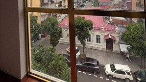 A room with a large window offering a view of a cityscape with buildings and parked cars. - Rio Batumi (Batumi)