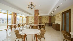 A spacious dining area with round tables and wicker chairs, a brick accent wall, and a large window offering a city view. - Rio Batumi (Batumi)